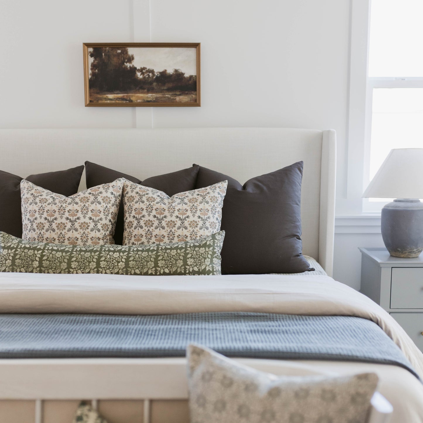 White bed with patterned and solid pillows in cream and black tones arranged against headboard.