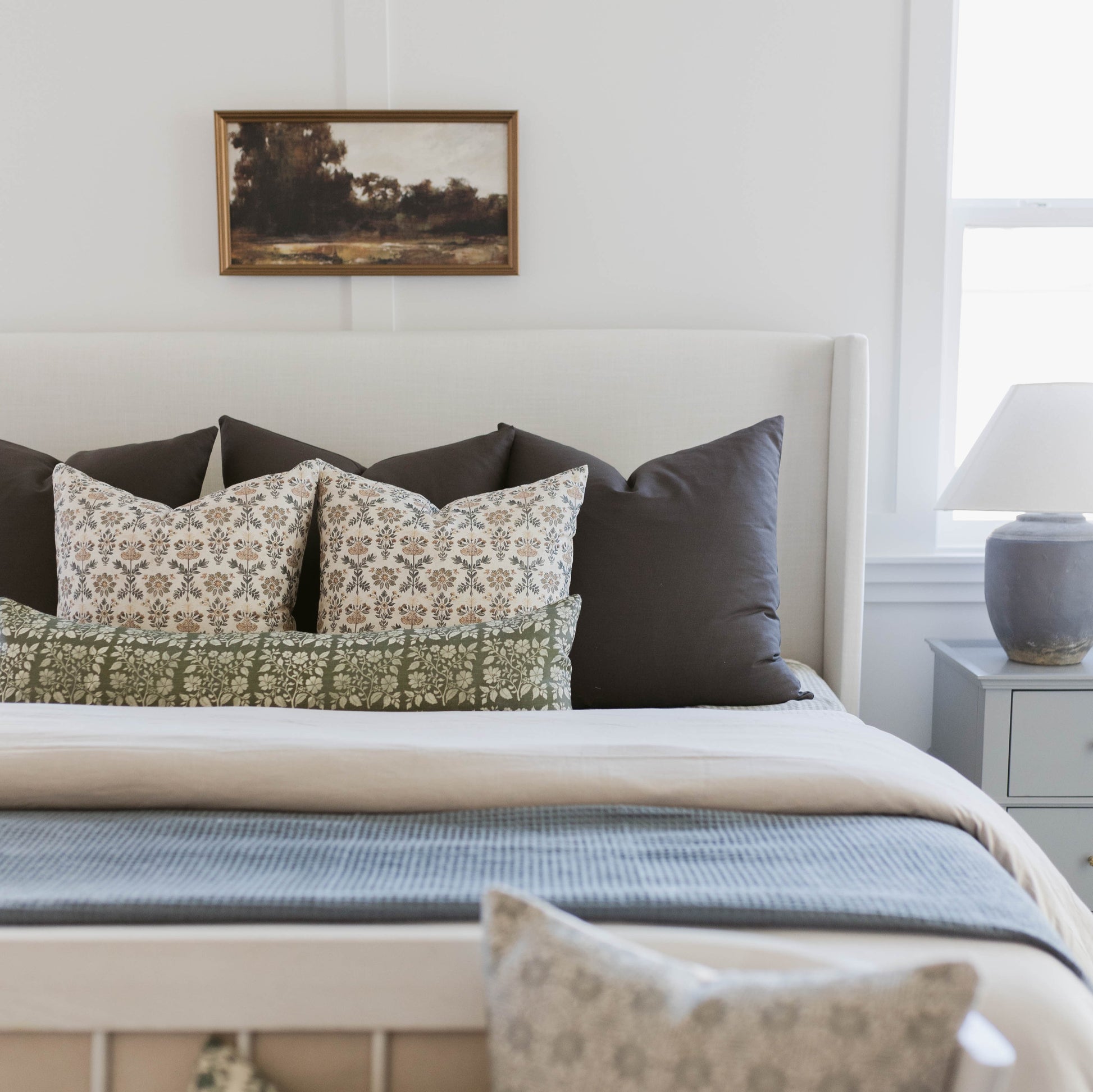 White bed with patterned and solid pillows in cream and black tones arranged against headboard.