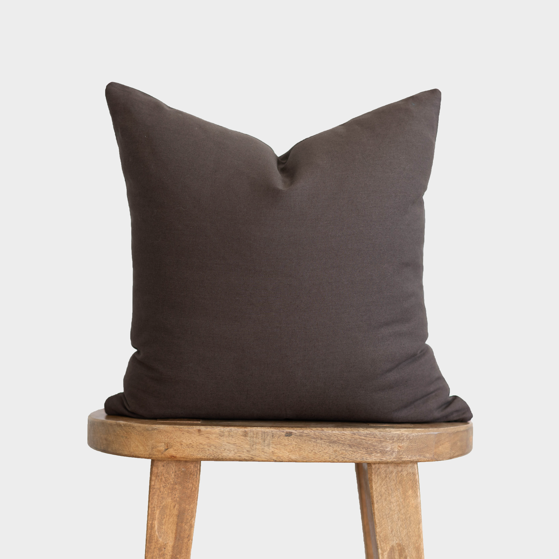 Charcoal gray double-sided pillow cover displayed on a wooden stool against a light gray background.