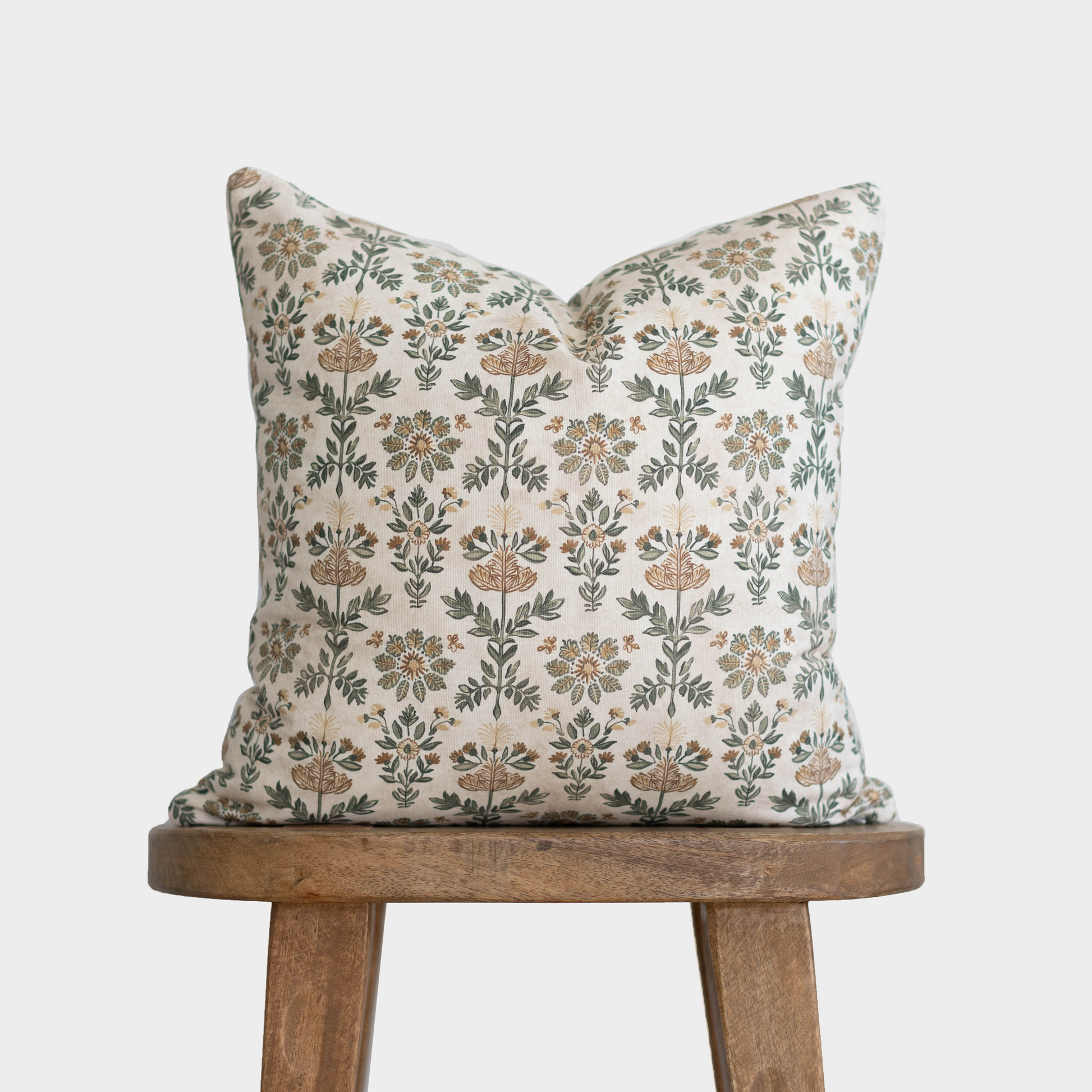 Cream linen pillow with tan and green floral botanical print pattern, displayed on wooden stool.