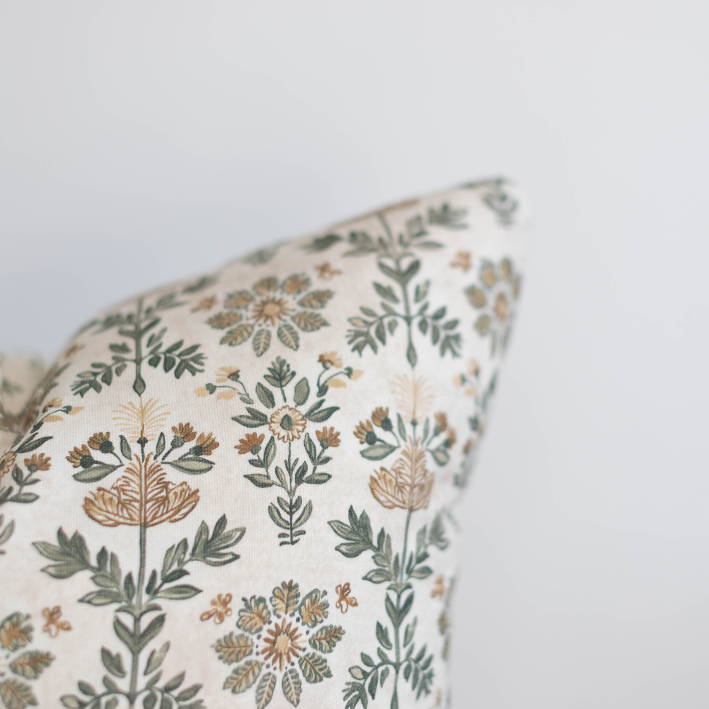Cream pillow with botanical print featuring tan and green stylized flowers and leaves.