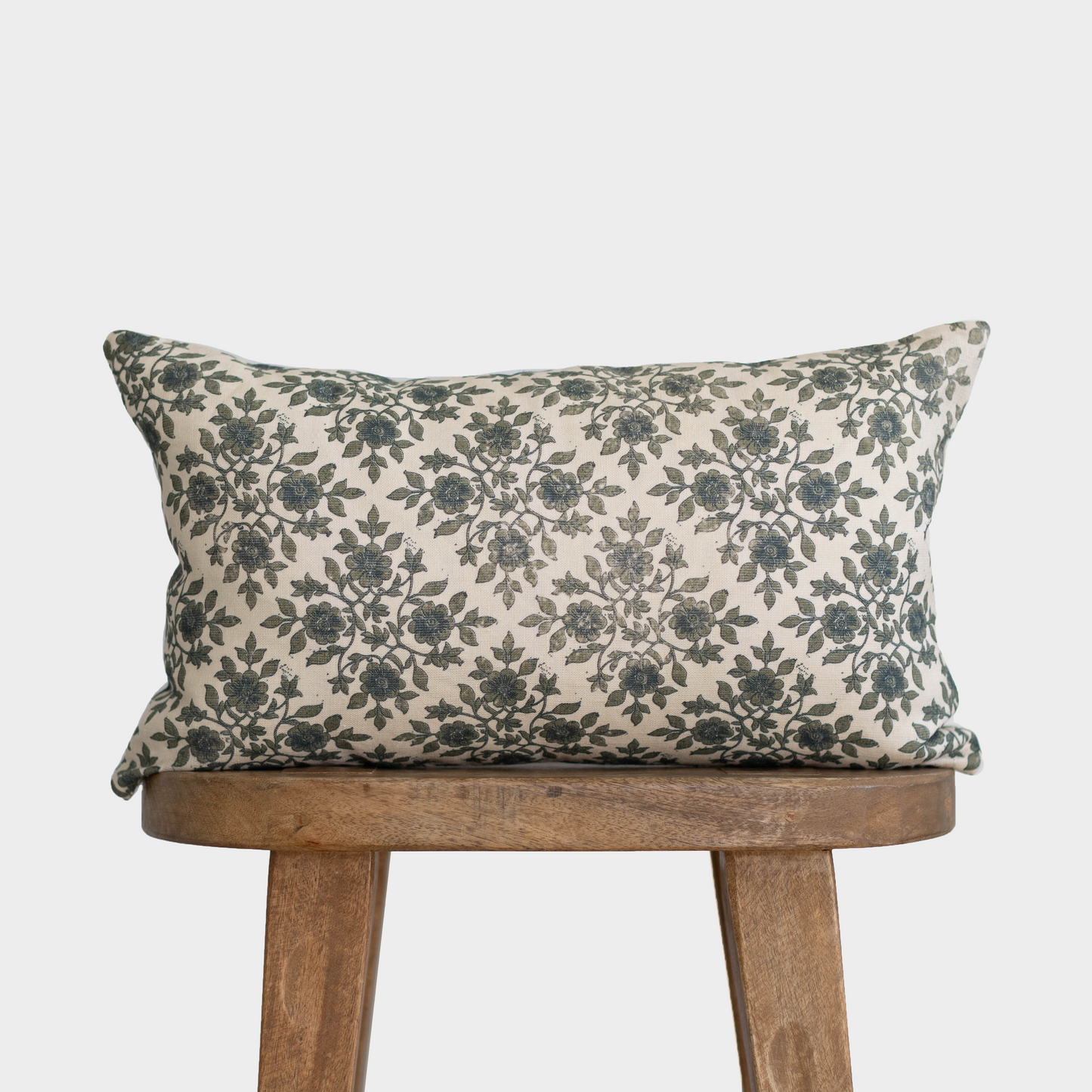 Cream lumbar pillow with dark green floral pattern, displayed on a wooden chair.