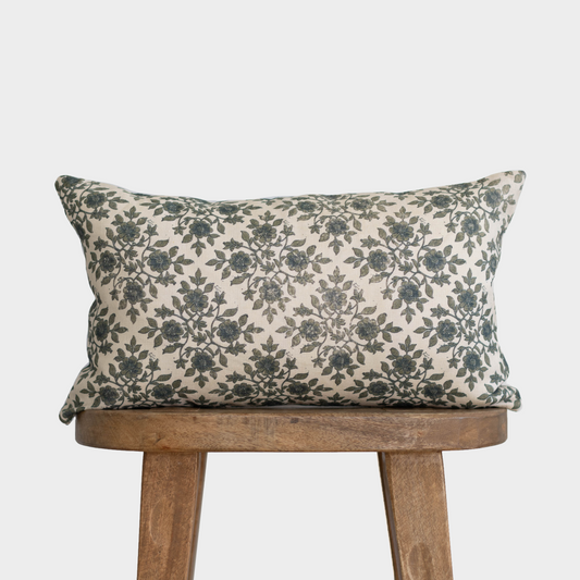 Cream lumbar pillow with dark green floral pattern, displayed on a wooden chair.
