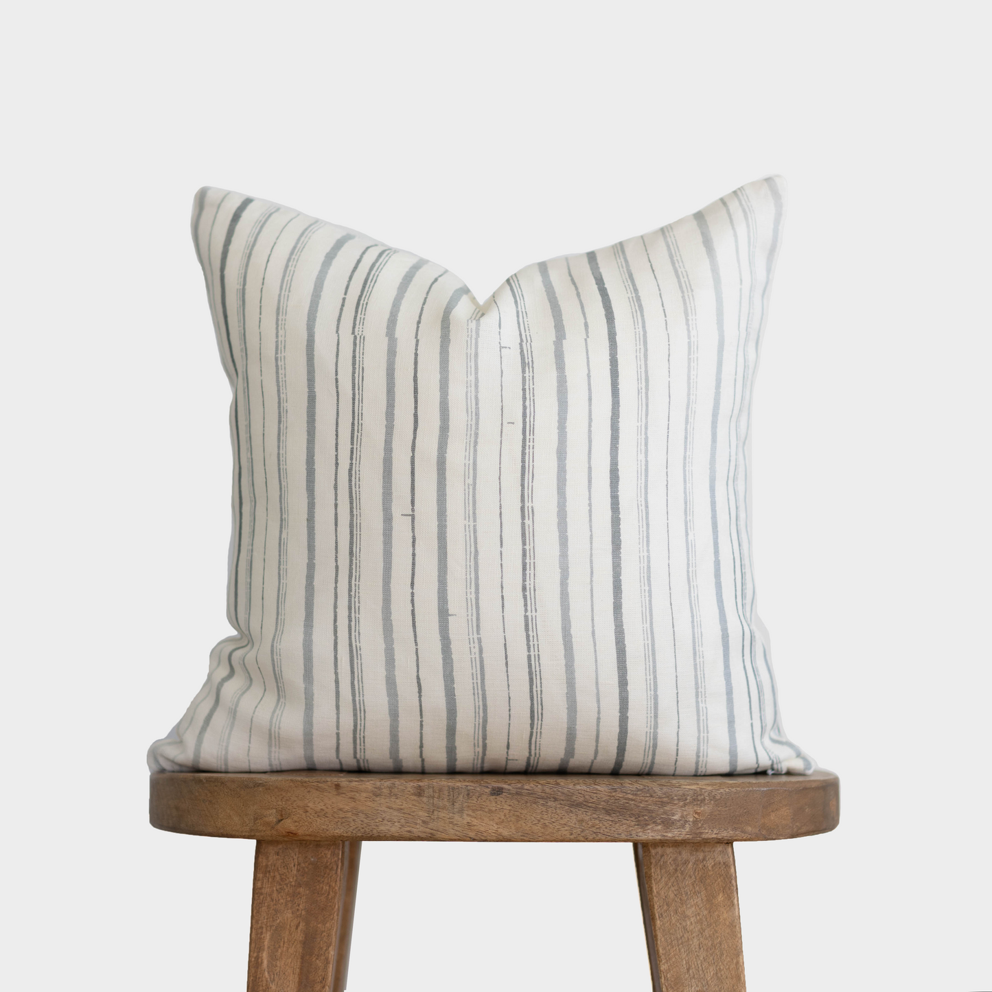 Cream linen pillow with gray vertical stripes on wooden stool.