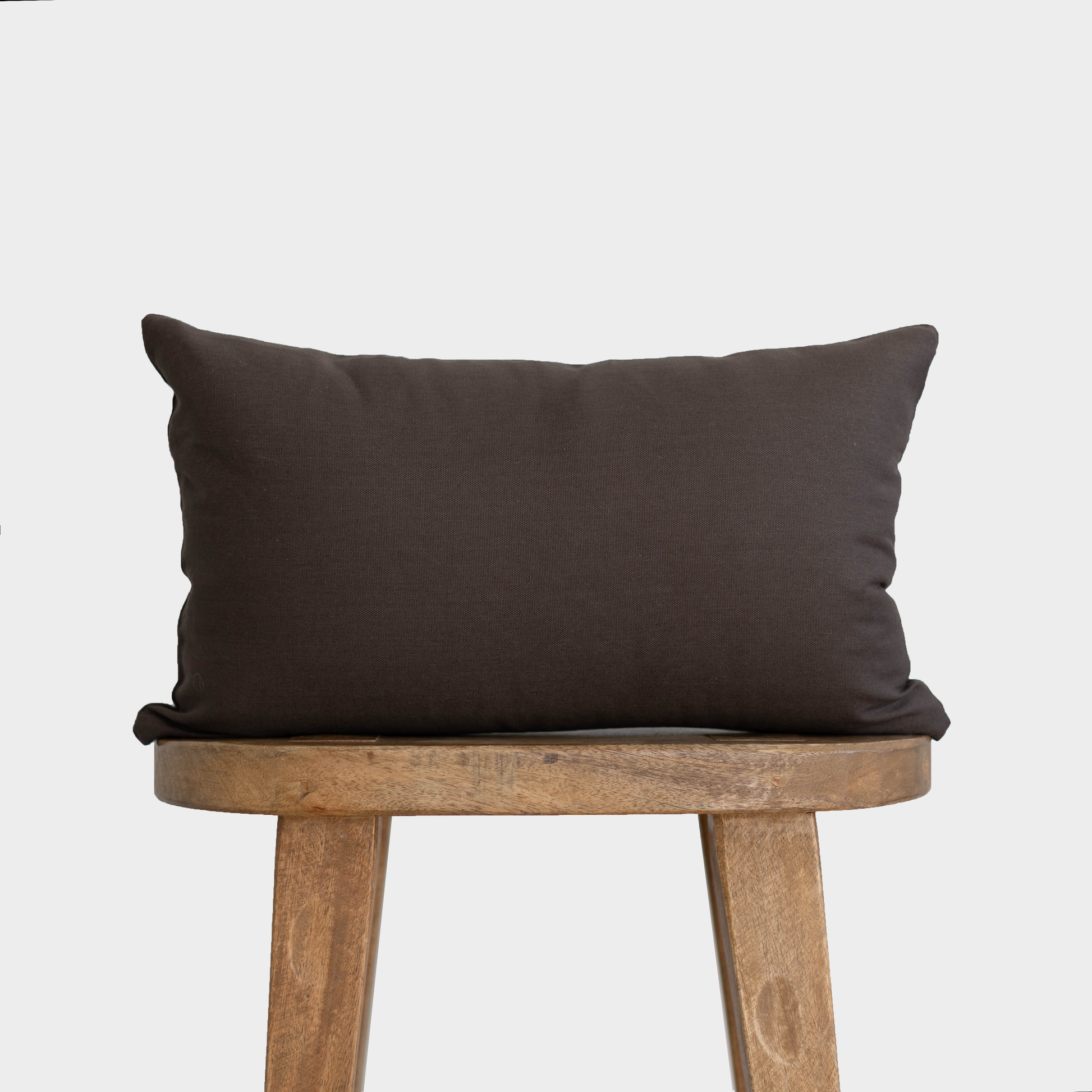 Dark gray double-sided lumbar pillow displayed on wooden chair seat.