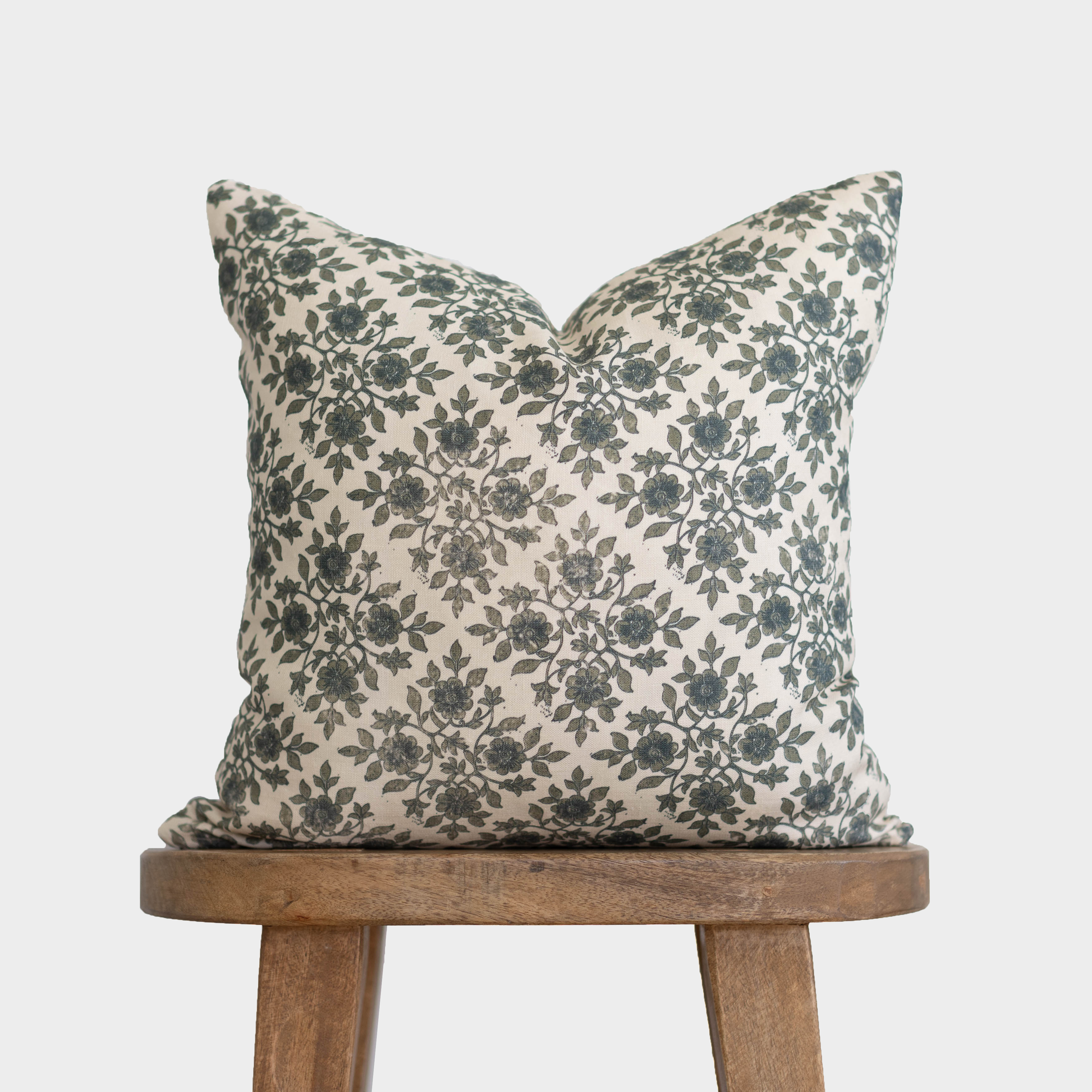 Cream linen pillow with dark green floral pattern, displayed on a wooden stool.