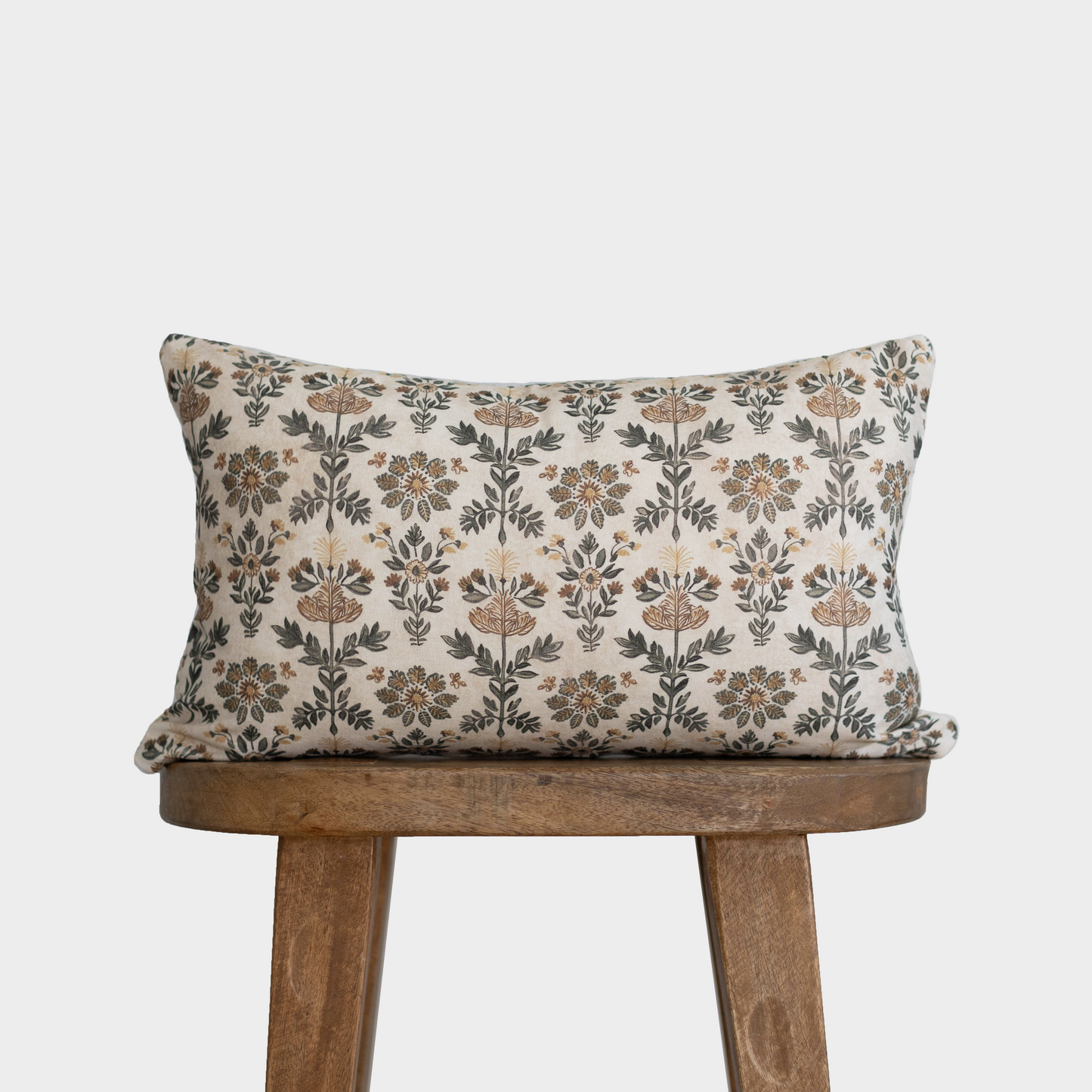 Rectangular pillow with cream background and brown botanical floral damask pattern on wooden stool.