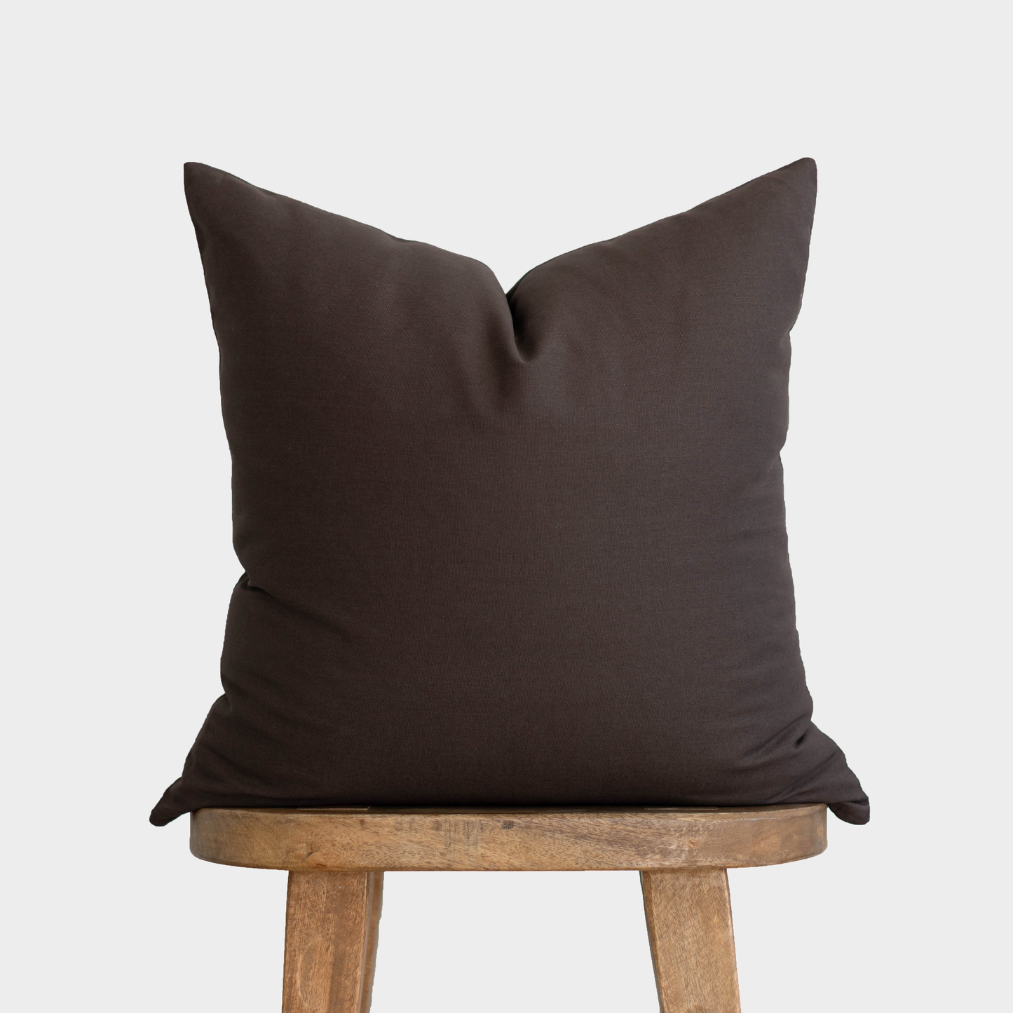 Dark brown double-sided pillow cover displayed on wooden stool legs.