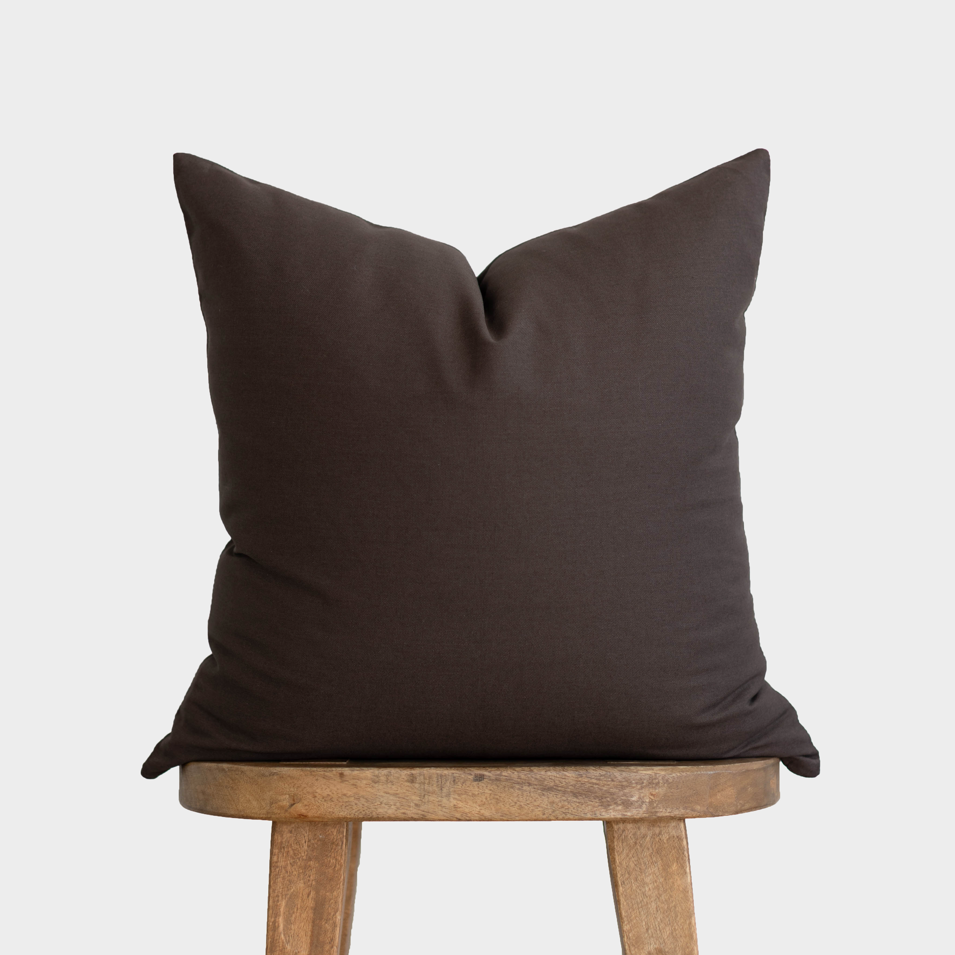 Dark brown double-sided pillow cover displayed on wooden stool legs.