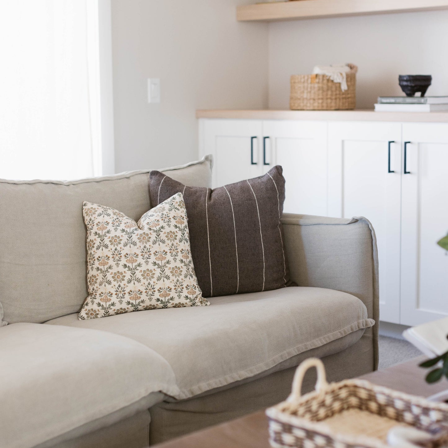 Beige upholstered sofa with rolled arms, styled with cream floral and charcoal striped throw pillows.