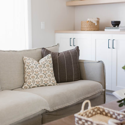 Beige upholstered sofa with rolled arms, styled with cream floral and charcoal striped throw pillows.