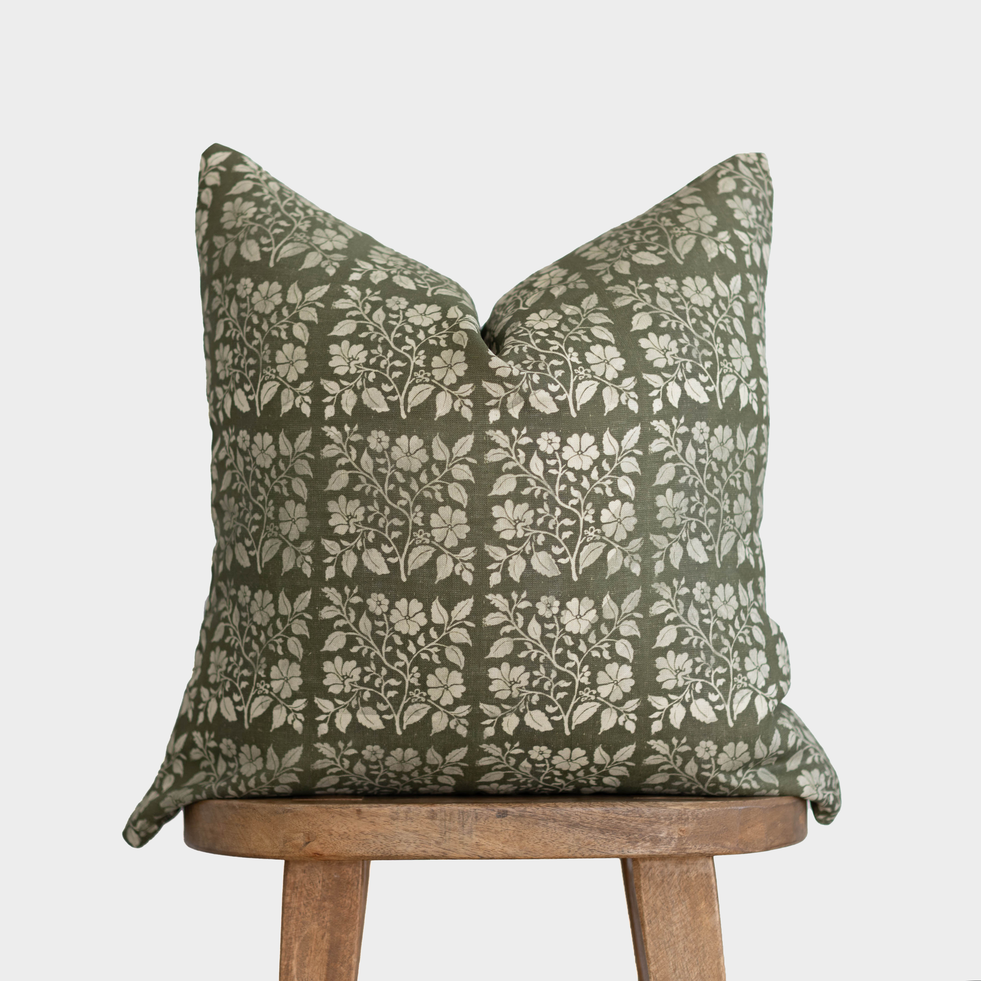 Sage green linen pillow with cream floral and leaf pattern, displayed on wooden stool.