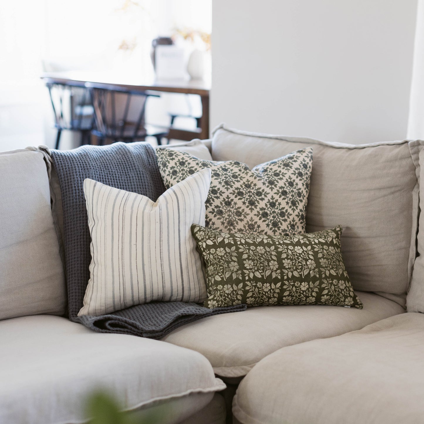 Linen pillow with olive green floral pattern displayed on beige sofa with coordinating pillows.