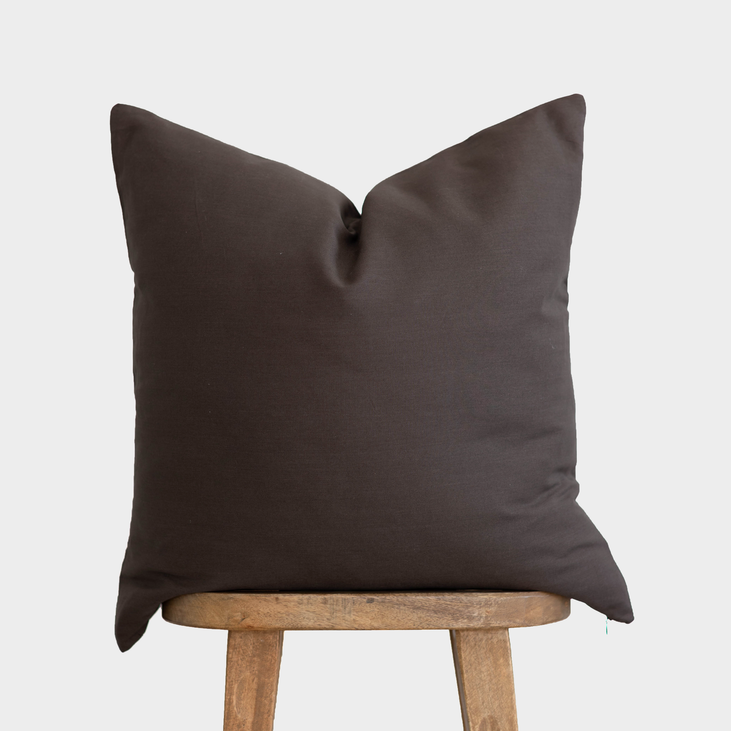 Dark brown double-sided pillow cover displayed on wooden stand against neutral background.