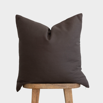 Dark brown double-sided pillow cover displayed on wooden stand against neutral background.