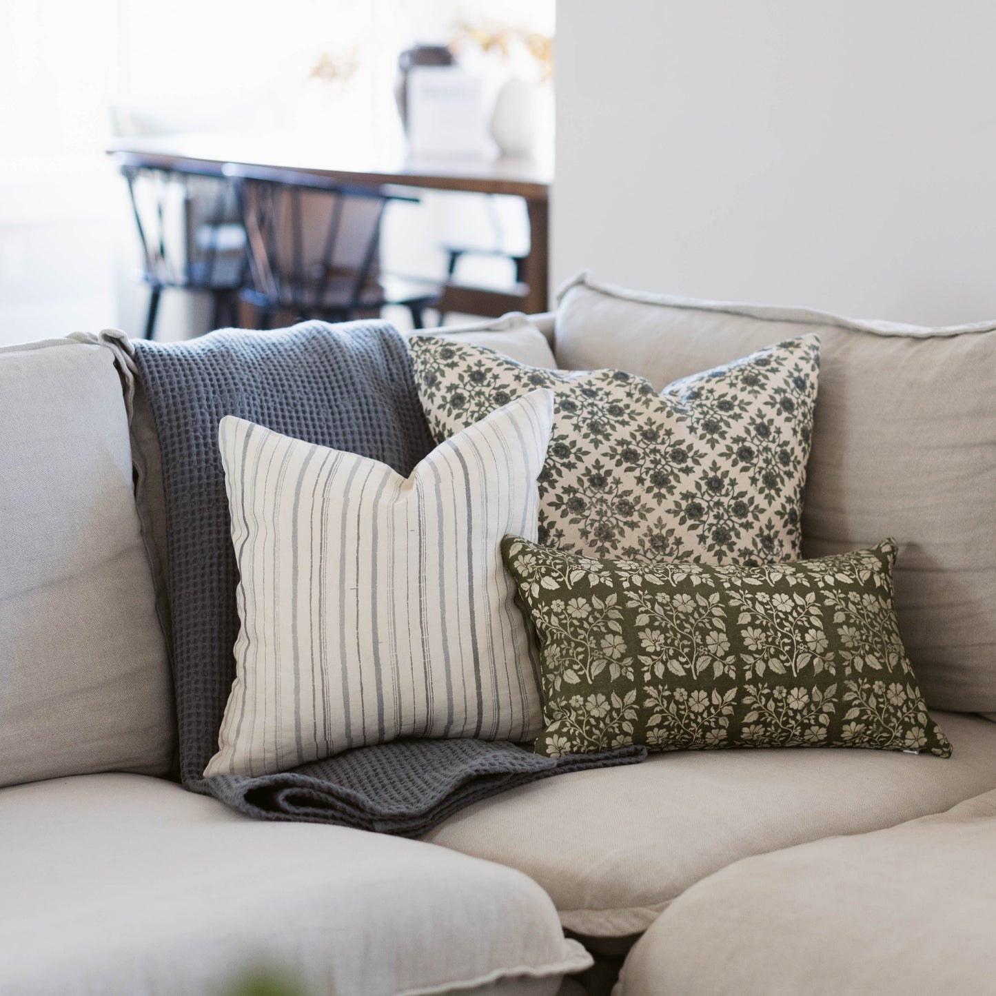 Beige linen pillow with striped, floral, and textured patterned accent pillows arranged on a light sofa.