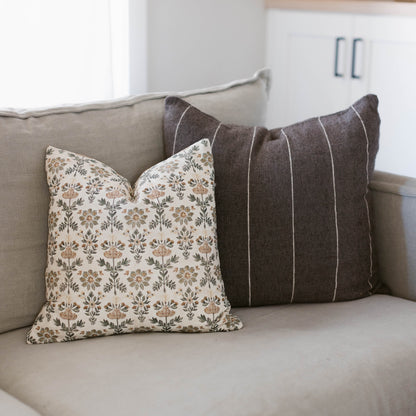 Two decorative pillows on a beige sofa: one with tan floral pattern, one with charcoal vertical stripes.