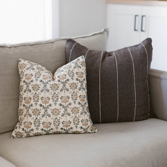 Two decorative pillows on a beige sofa: one with tan floral pattern, one with charcoal vertical stripes.