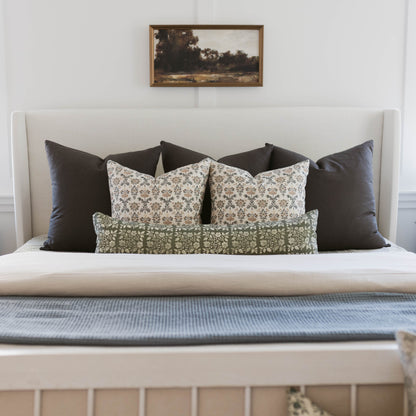 Bed styled with black and patterned pillows in cream and green tones against a light upholstered headboard.
