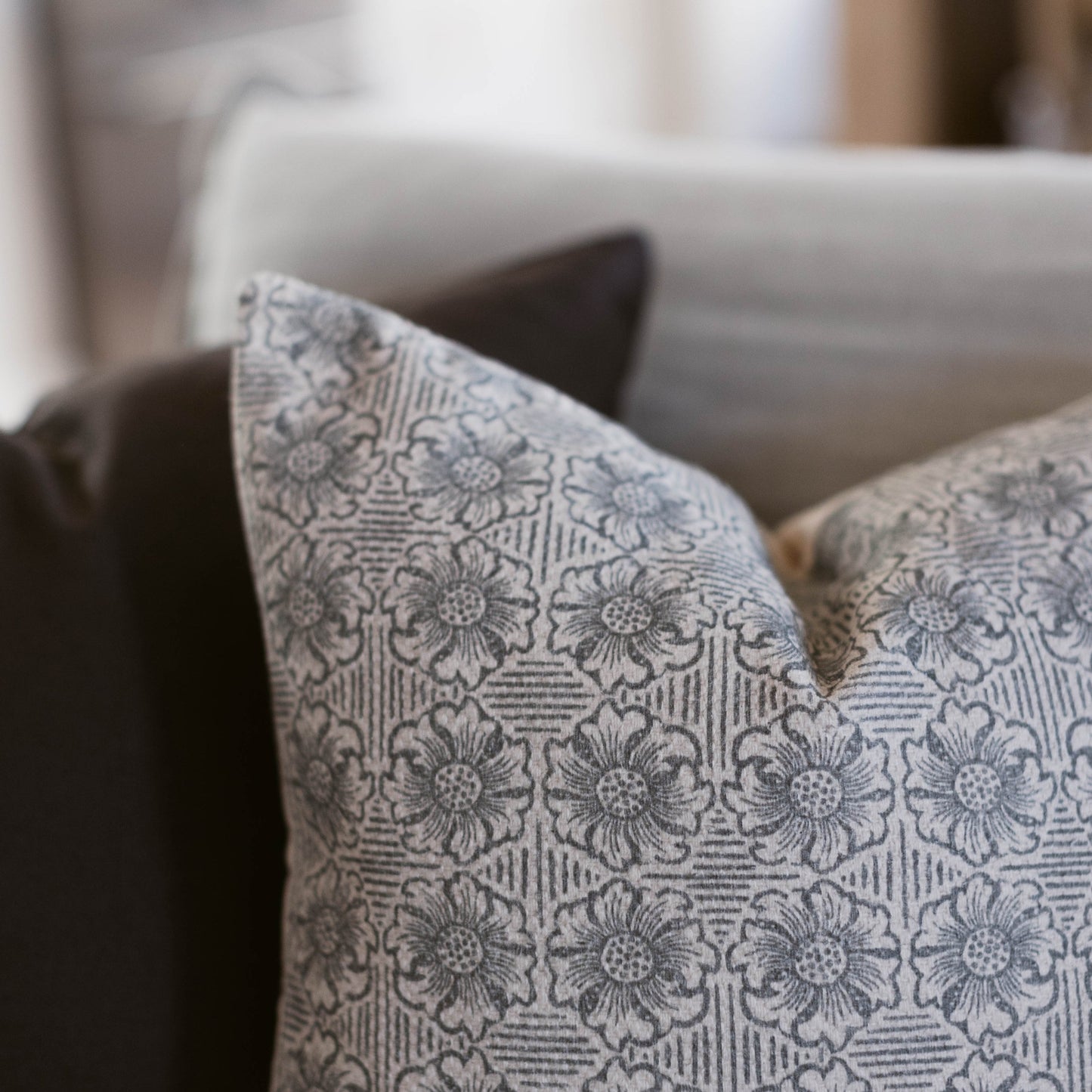 Cream and gray throw pillow with floral damask pattern displayed on a gray sofa.