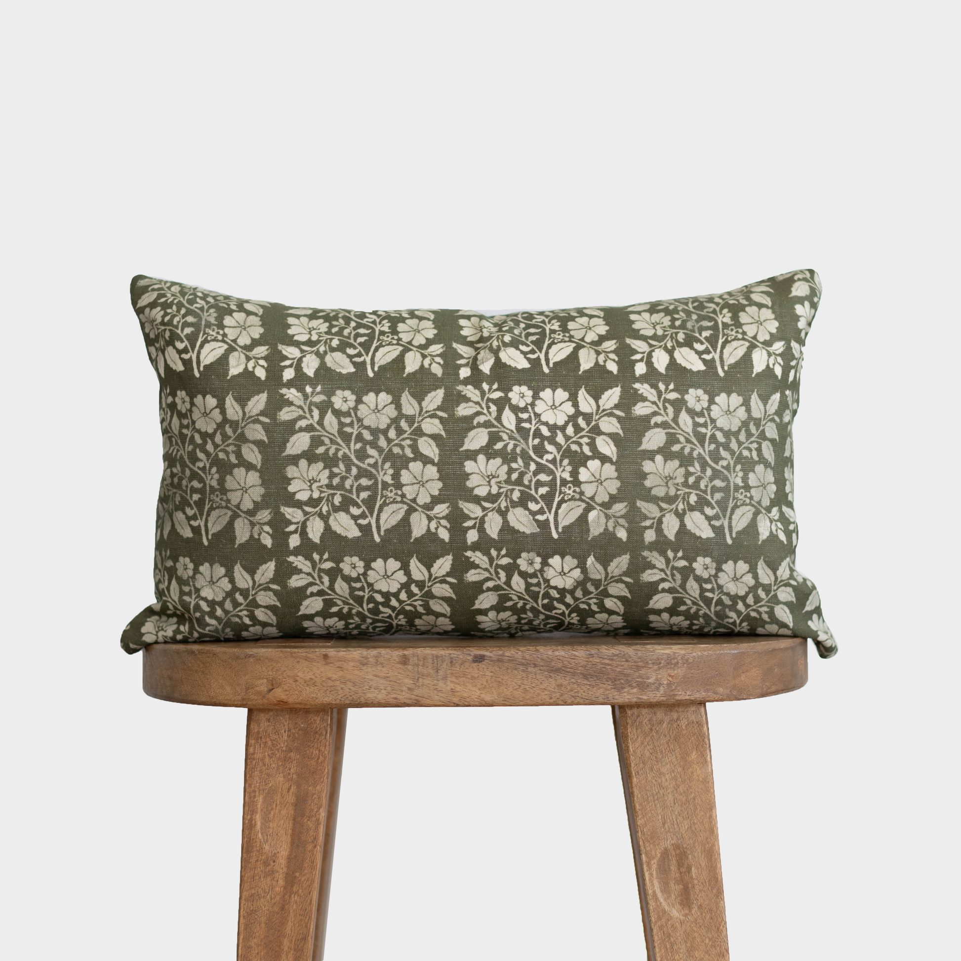 Rectangular linen lumbar pillow with green and cream floral vine pattern, displayed on wooden stool.