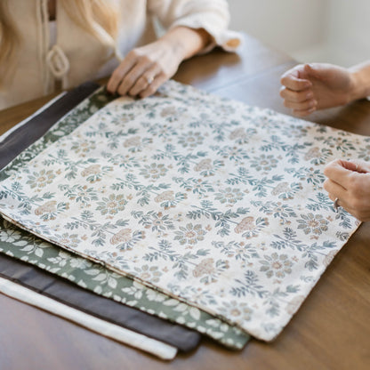 Four fabric swatches in varying sizes displaying floral and botanical prints in blue, gray, and neutral tones.