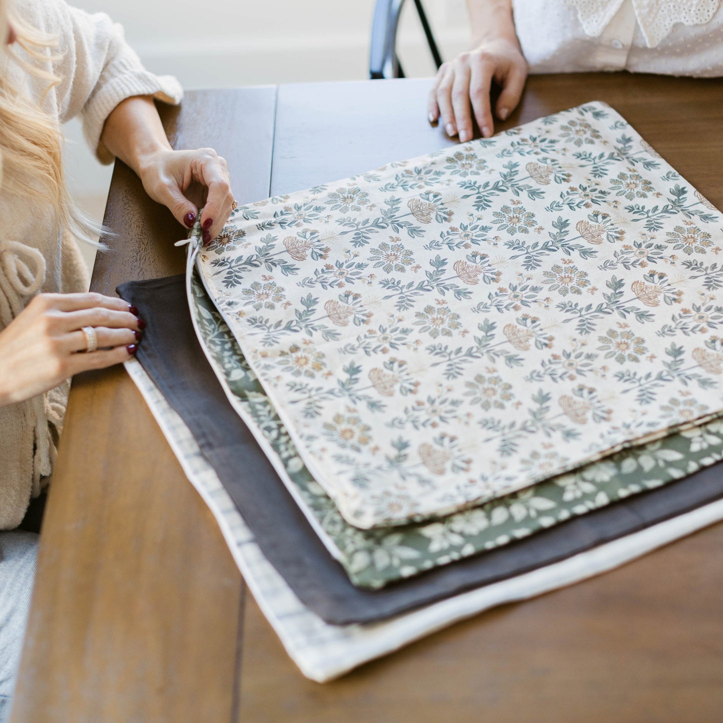 Stack of four fabric swatches with floral and geometric patterns in cream, green, and blue tones.