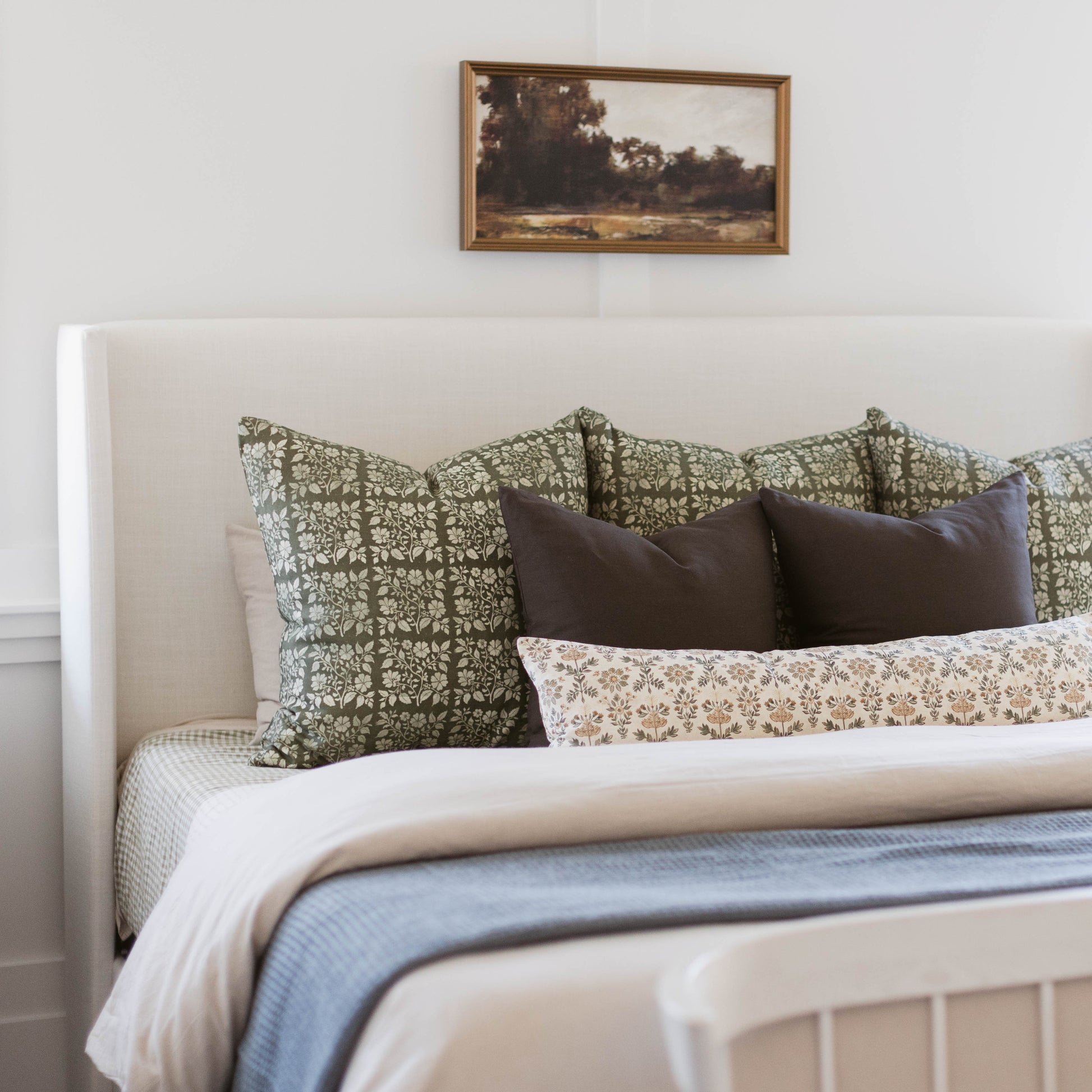 Decorative linen pillow with green and cream floral damask pattern displayed on bed with coordinating pillows.