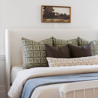 Decorative linen pillow with green and cream floral damask pattern displayed on bed with coordinating pillows.