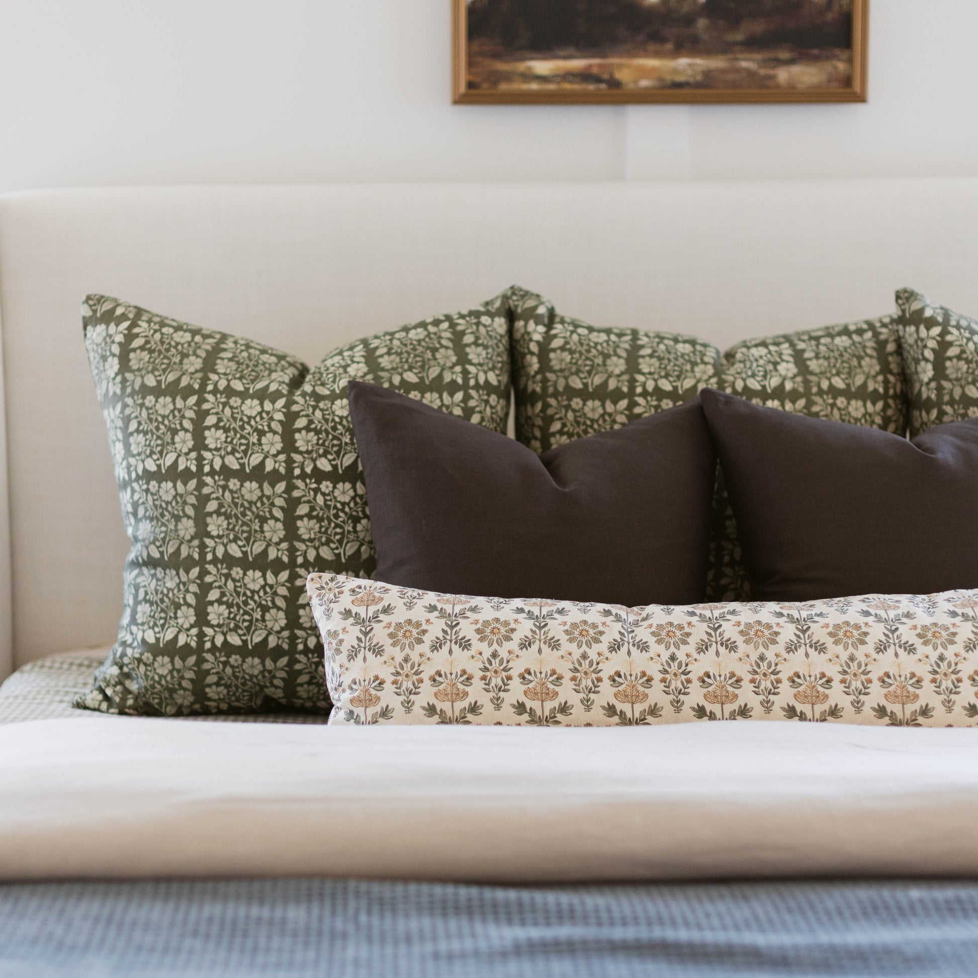 Bed styled with green floral, brown, and tan patterned pillows against white upholstered headboard.