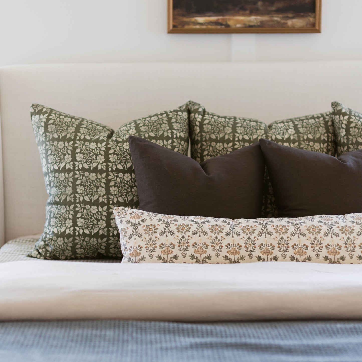 Linen pillow with white and tan botanical floral pattern in evergreen and natural tones on bed.