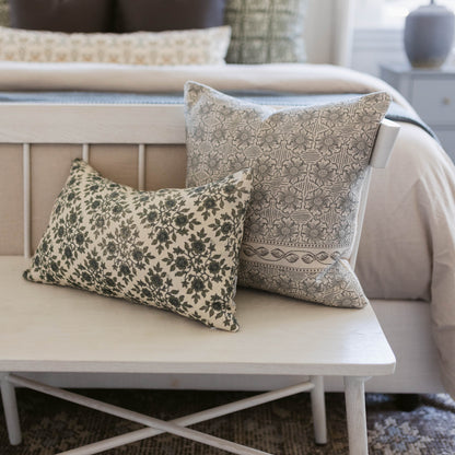 Two decorative pillows with damask and floral patterns in cream and sage tones displayed on a white wooden bench.