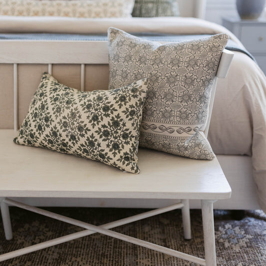 Two rectangular lumbar pillows with geometric and floral patterns in cream and sage green on a white bench.