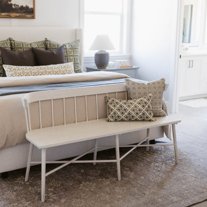 Tan and cream patterned lumbar pillow displayed on a white wooden bench at the foot of a bed.