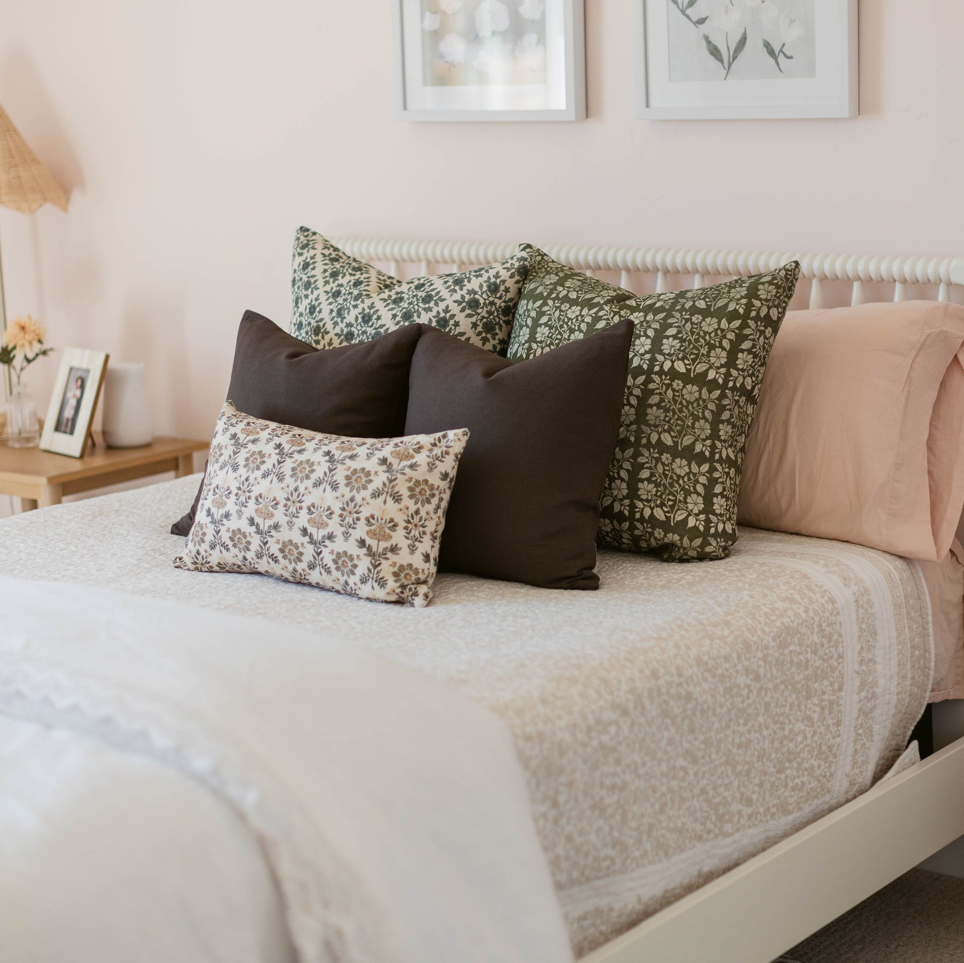 Linen pillows with floral and botanical prints in green, cream, and brown tones arranged on a bed.