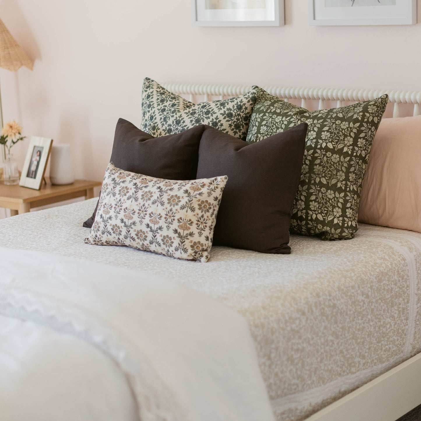 Fannie pillow set arranged on bed with green floral, black, and cream patterned cushions in various sizes.