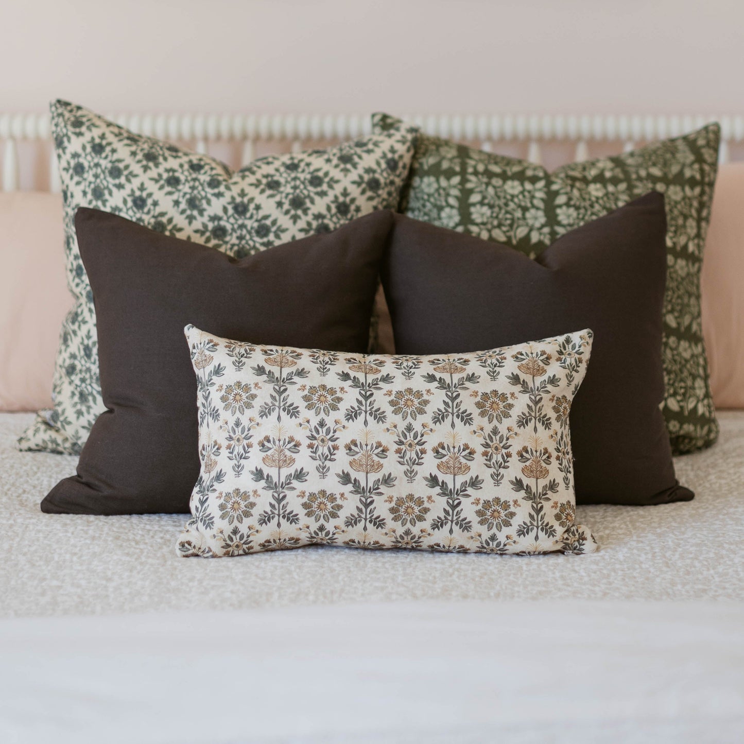 Three decorative pillows with damask and floral patterns in cream, green, and charcoal displayed on a bed.