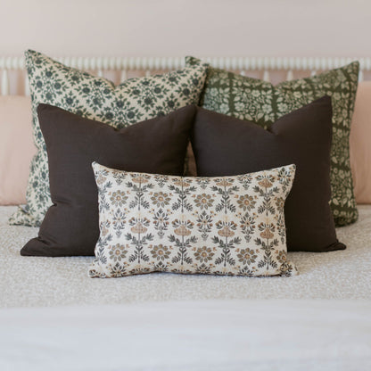 Three decorative pillows with damask and floral patterns in cream, green, and charcoal displayed on a bed.