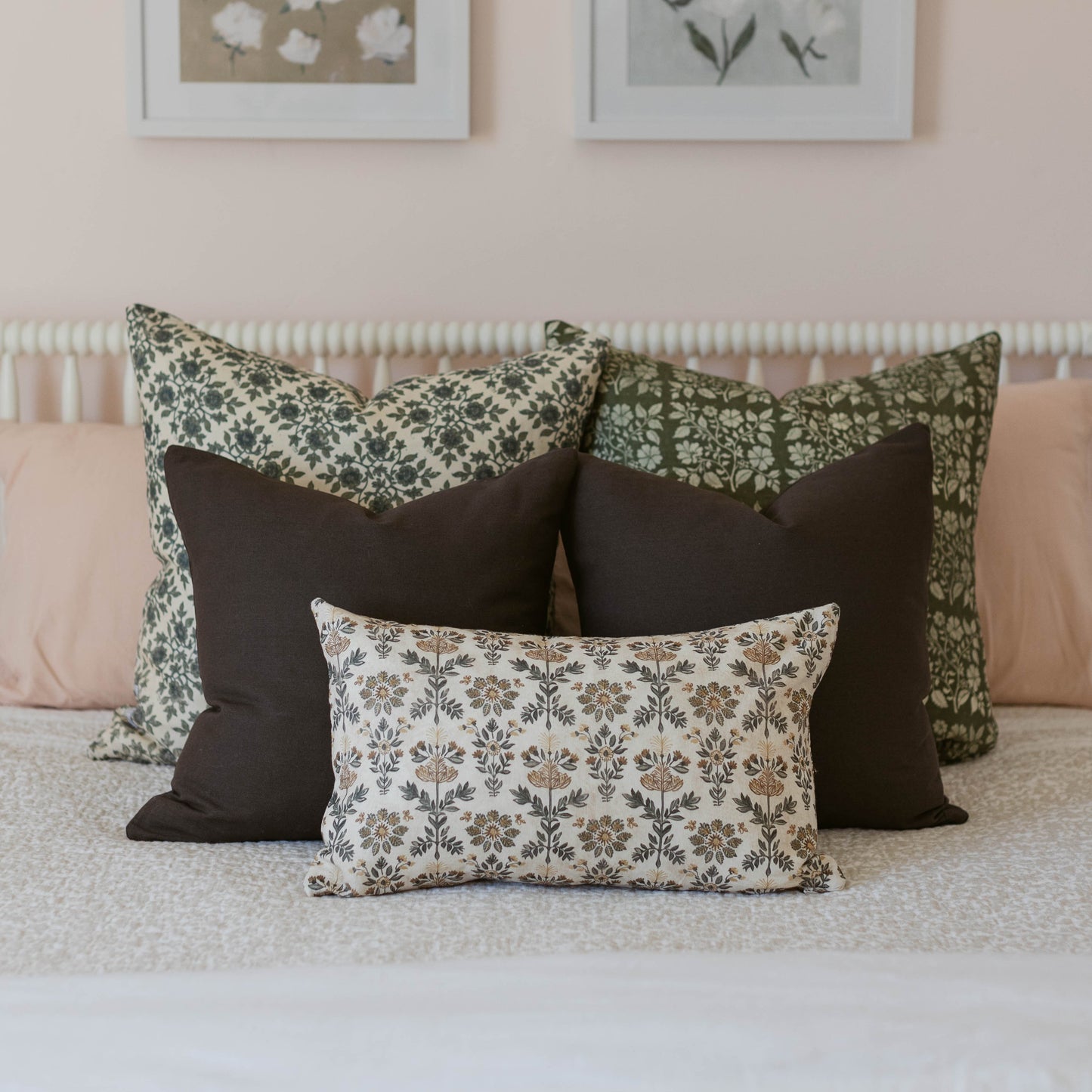 Three decorative pillows with floral and geometric patterns in green, black, and cream arranged on a bed.