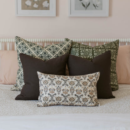Three decorative pillows with floral and geometric patterns in green, black, and cream arranged on a bed.