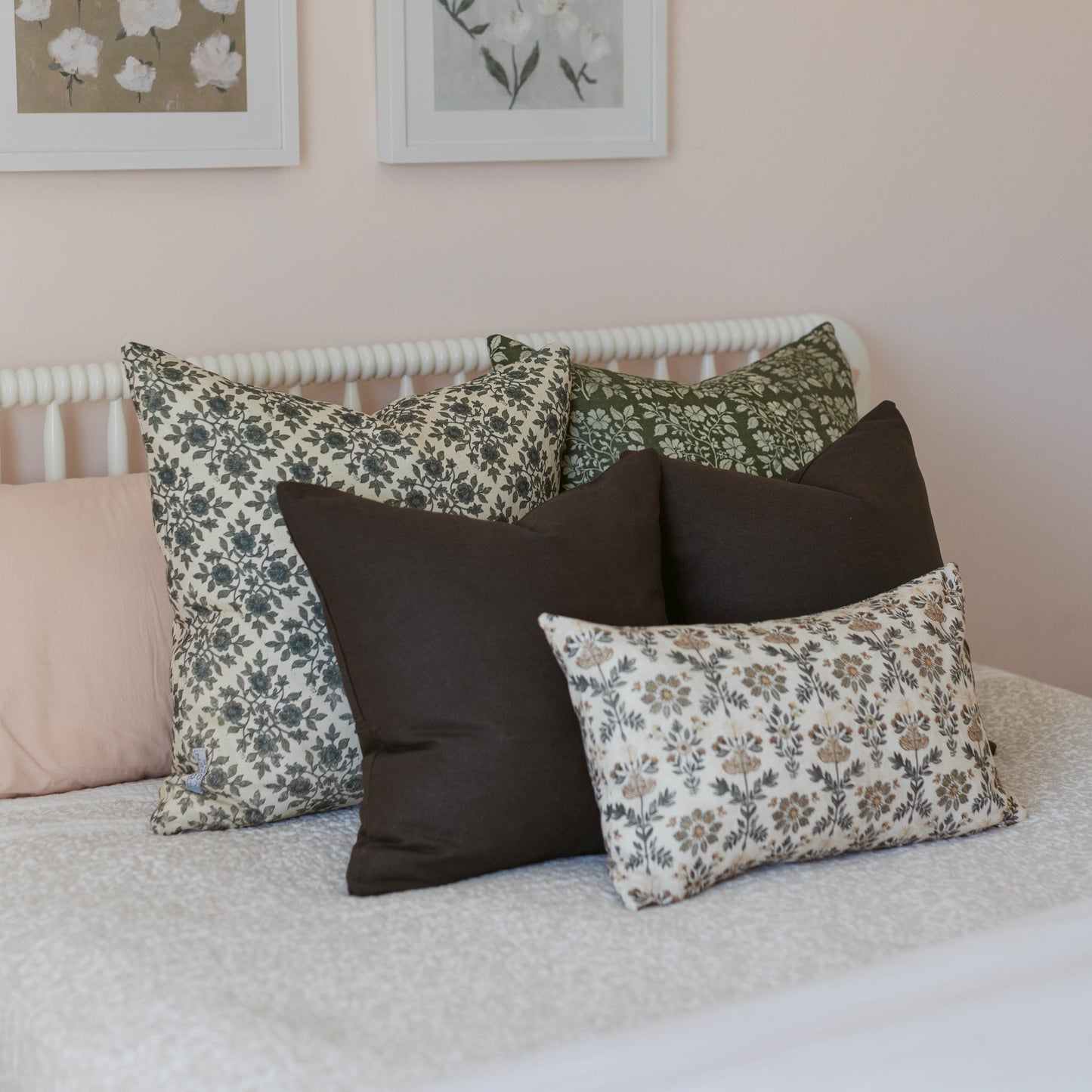 Assorted double-sided throw pillows with floral and solid patterns in green, black, and cream arranged on a bed.