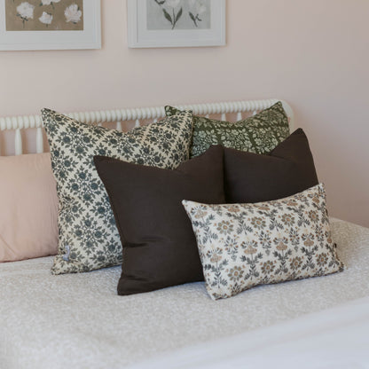 Five decorative pillows arranged on a bed: two patterned pillows in sage and cream, two solid black pillows, and one cream pi