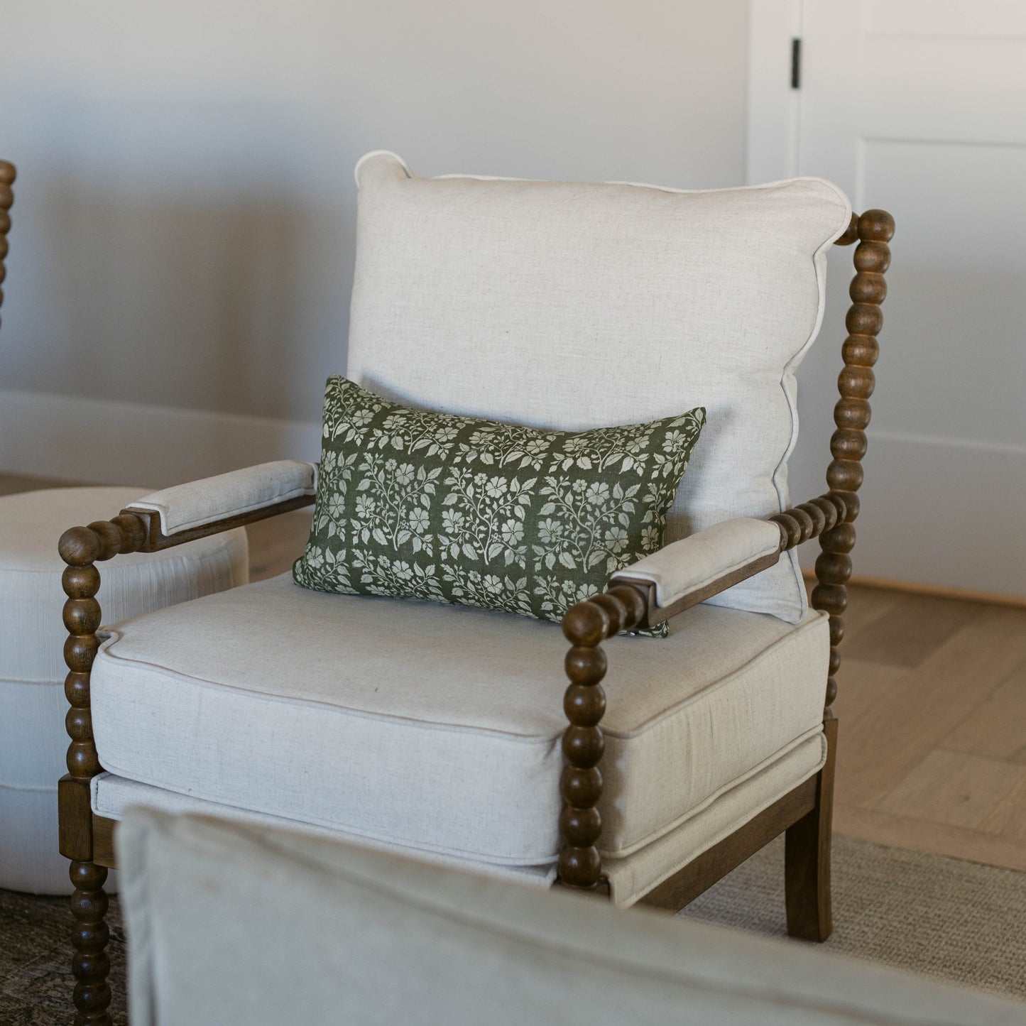 Lumbar pillow with olive green floral pattern on cream linen, displayed on upholstered chair.