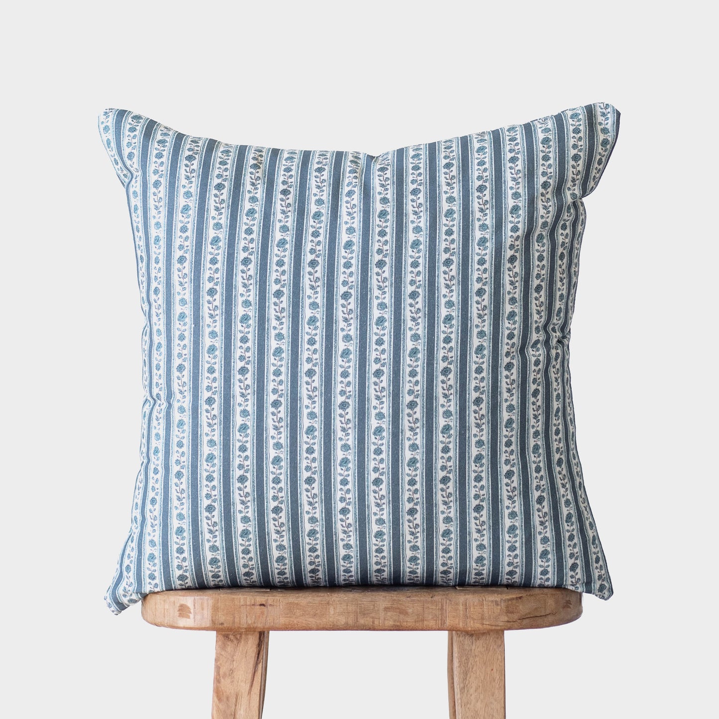 Blue and white striped decorative pillow with floral motif placed on wooden stool.