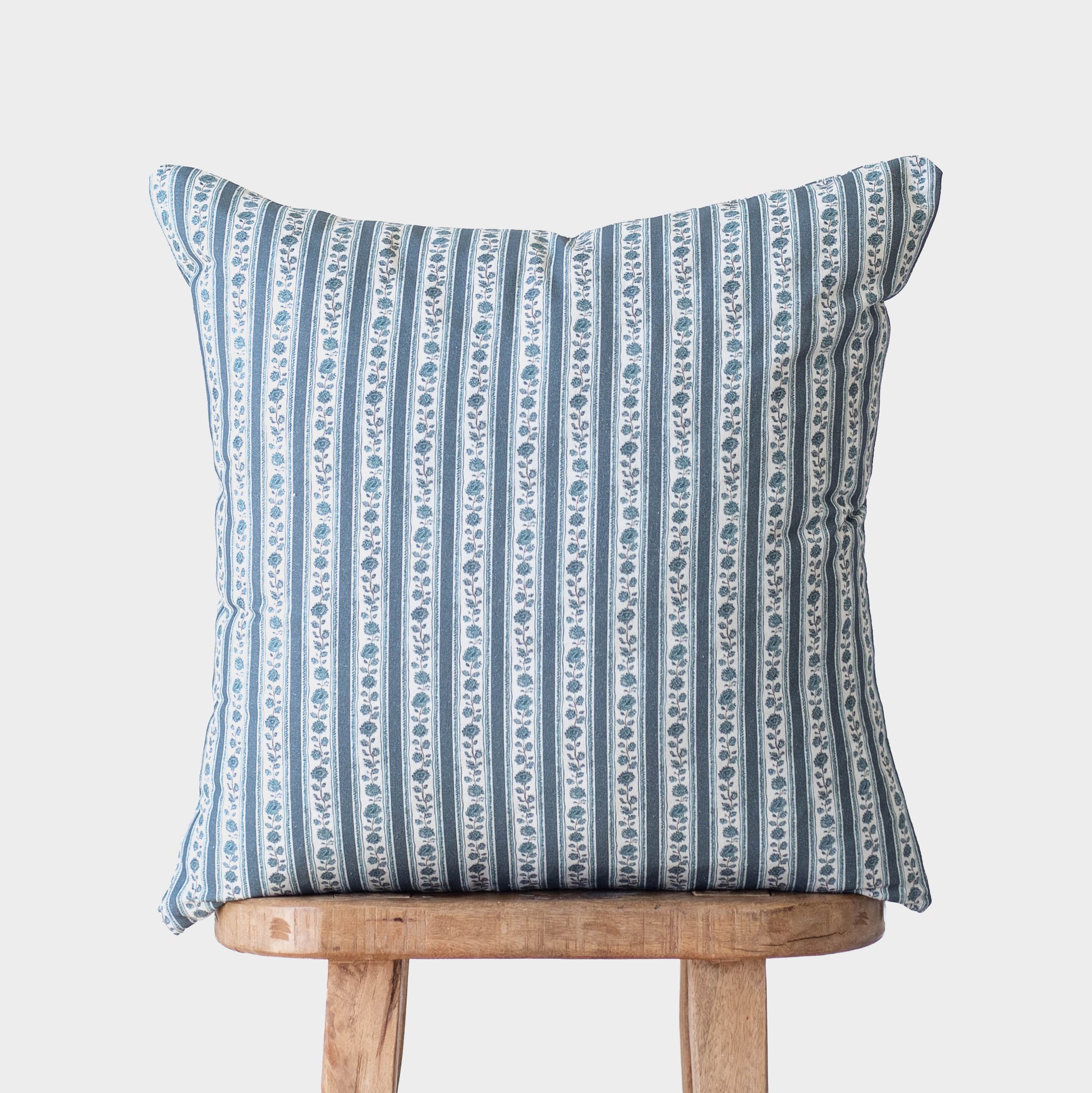 Blue and white striped decorative pillow with floral motif placed on wooden stool.