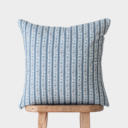 Blue and white striped decorative pillow with floral motif placed on wooden stool.