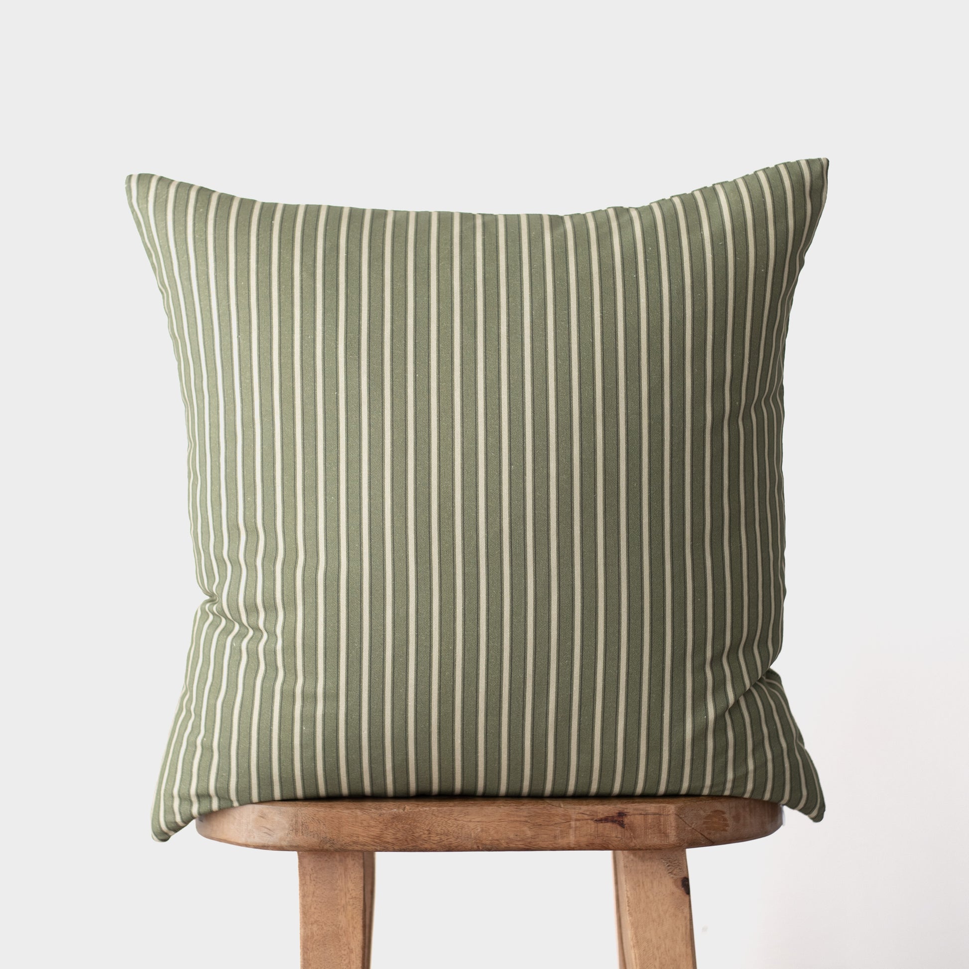 Sage green and cream striped throw pillow on wooden stool against neutral background.