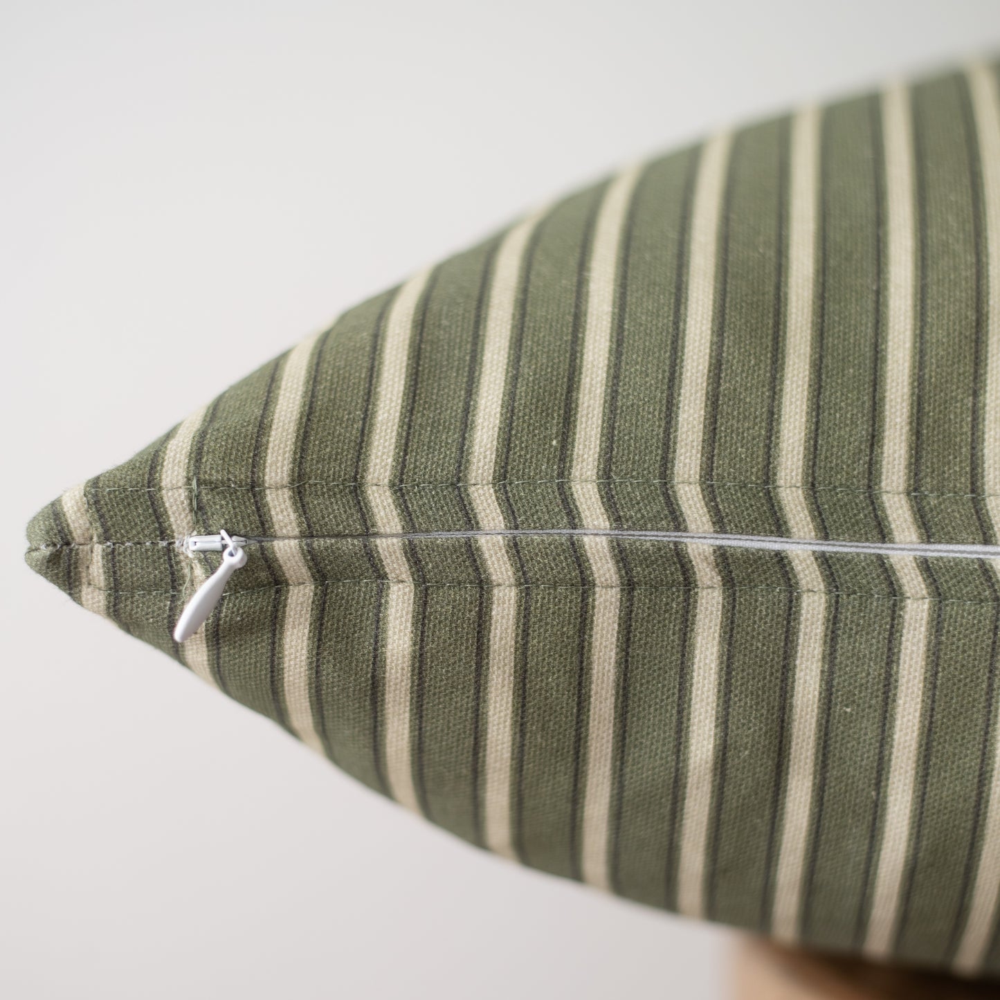 Sage green and cream striped pillow with white zipper closure, angled view.