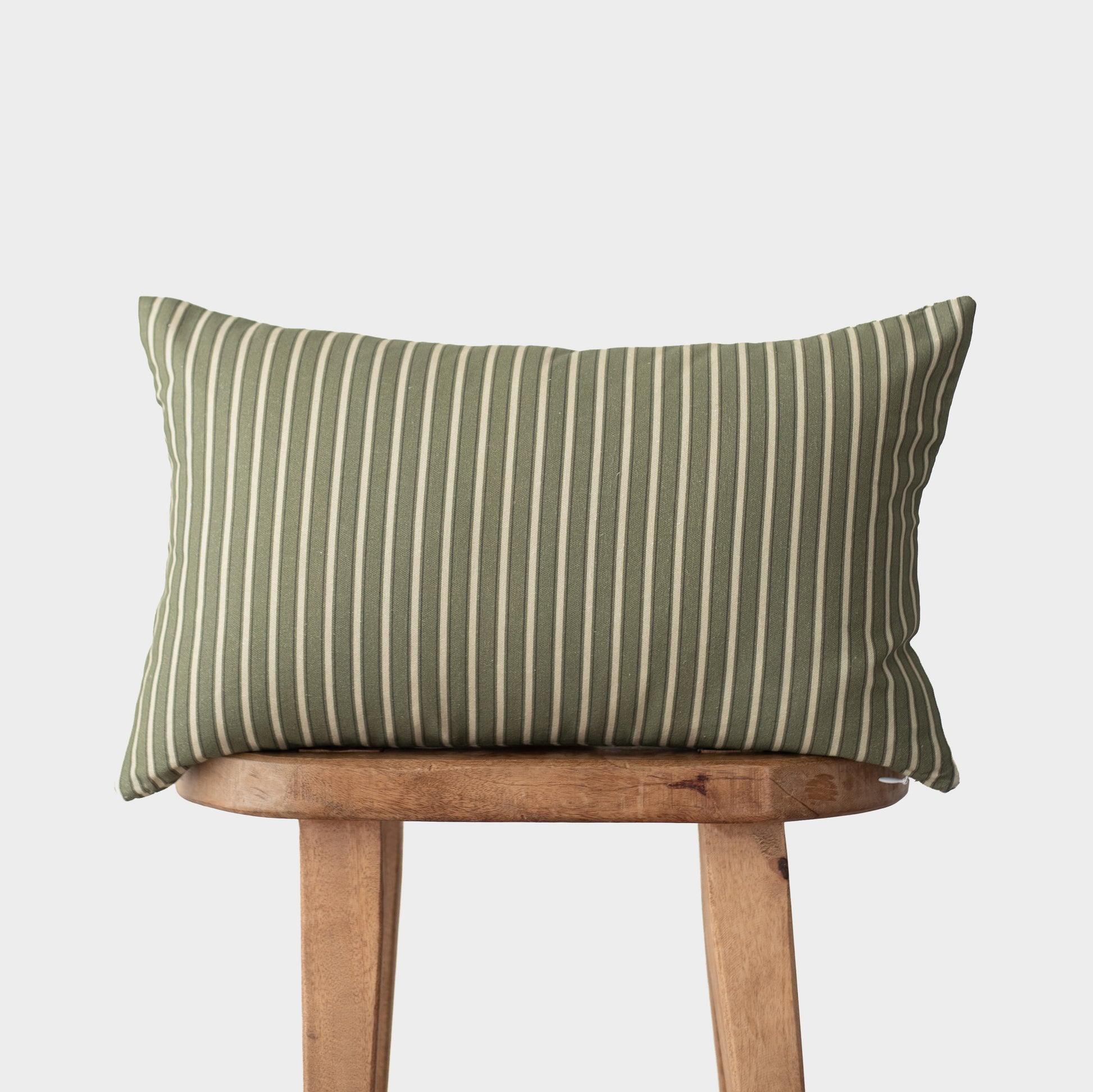 Sage green and cream striped lumbar pillow displayed on wooden chair back against white background.