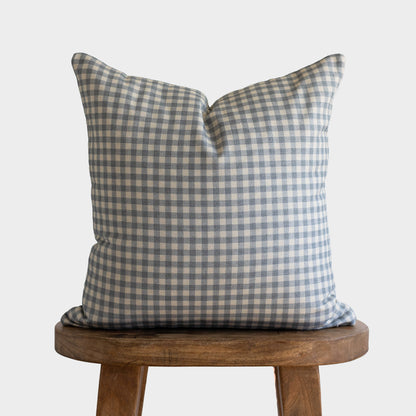 Dusty blue and white gingham check pillow displayed on a wooden stool.